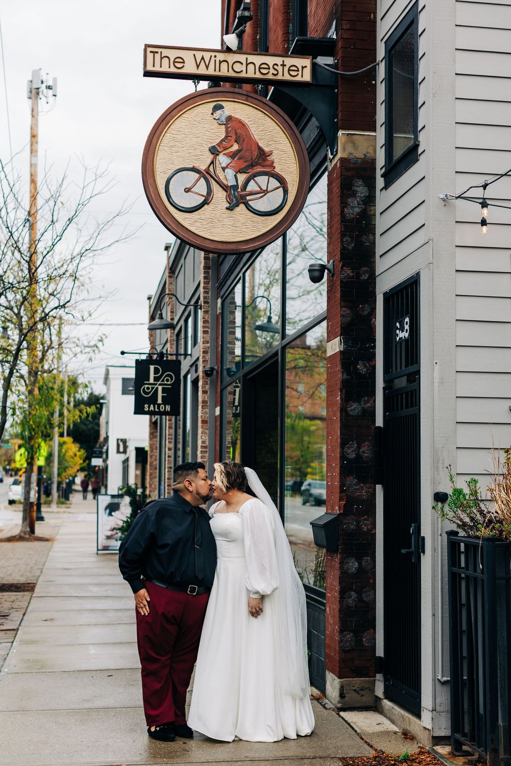 A couple shares an intimate moment under a vintage bicycle sign outside The Winchester restaurant.