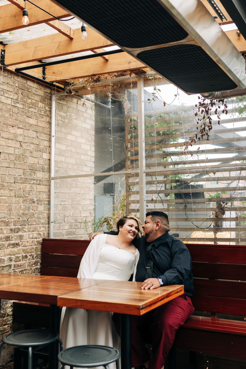 A couple sharing an intimate moment at a table with natural light streaming through window blinds.