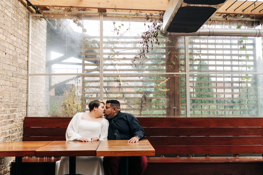 A couple sharing a romantic moment at a restaurant table near a window with natural light.