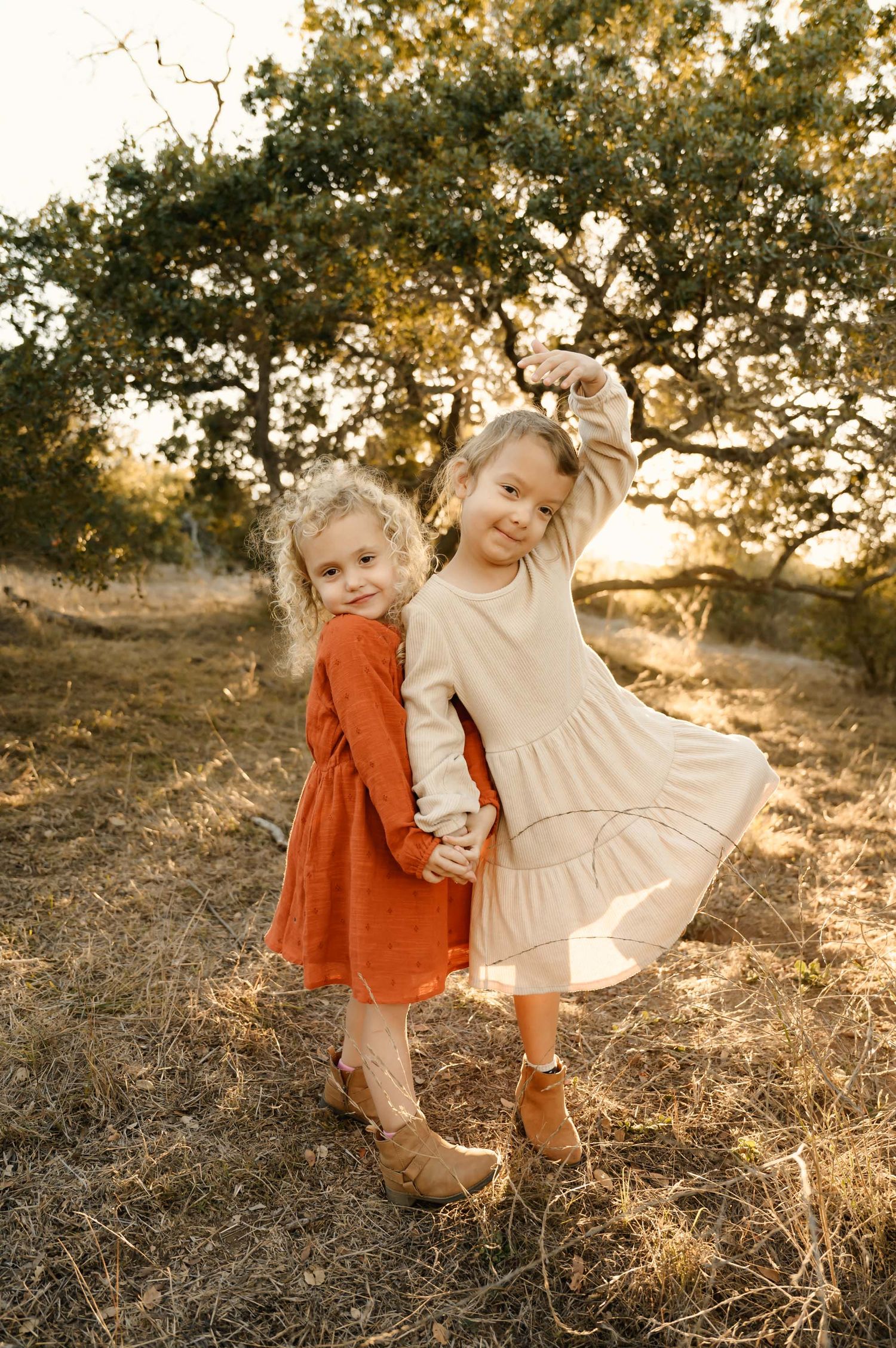Two children holding hands in a sunlit field with trees in the background.