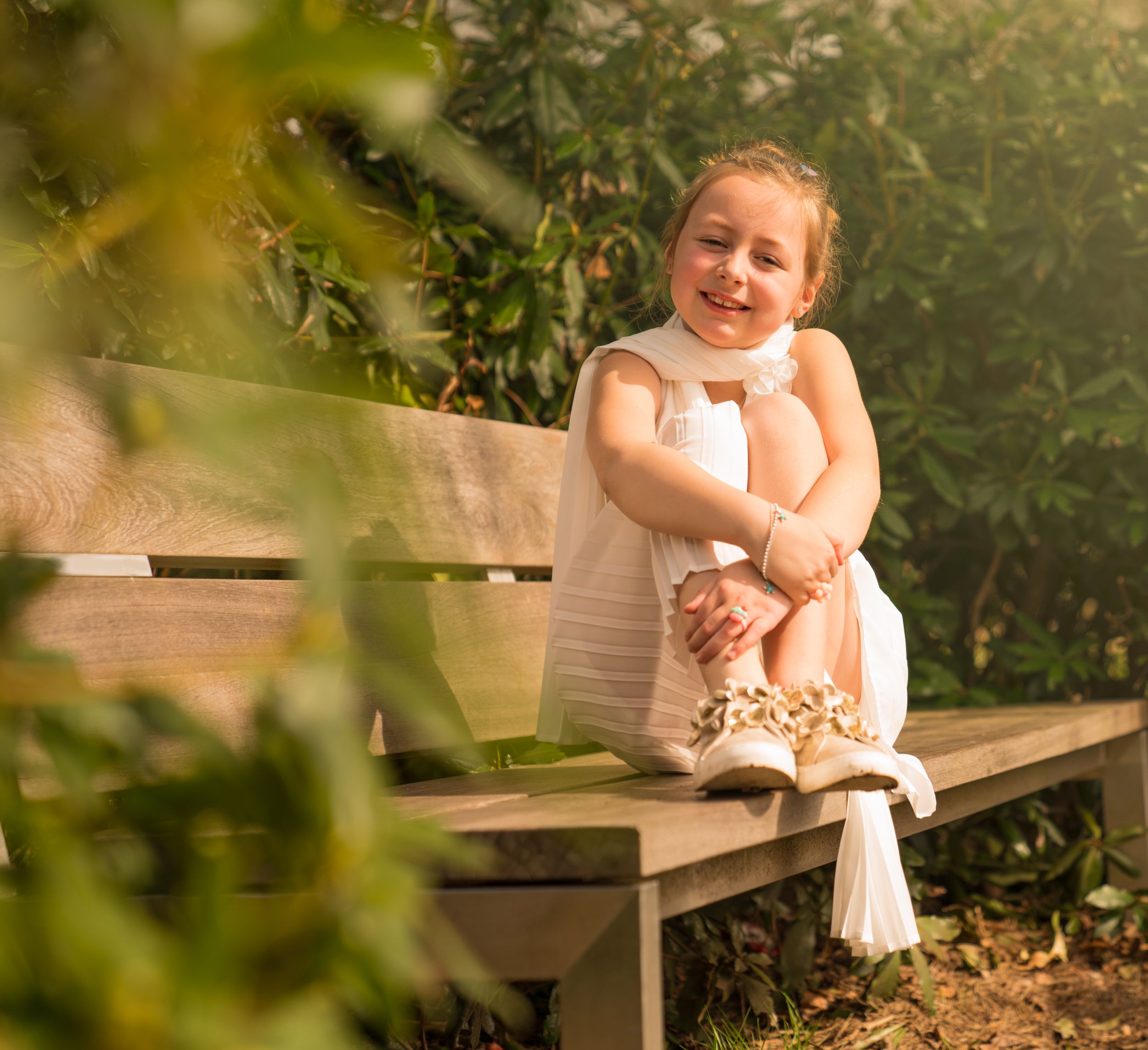 een foto van een meisje (communicant) op een bankje in het zonlicht in een park.