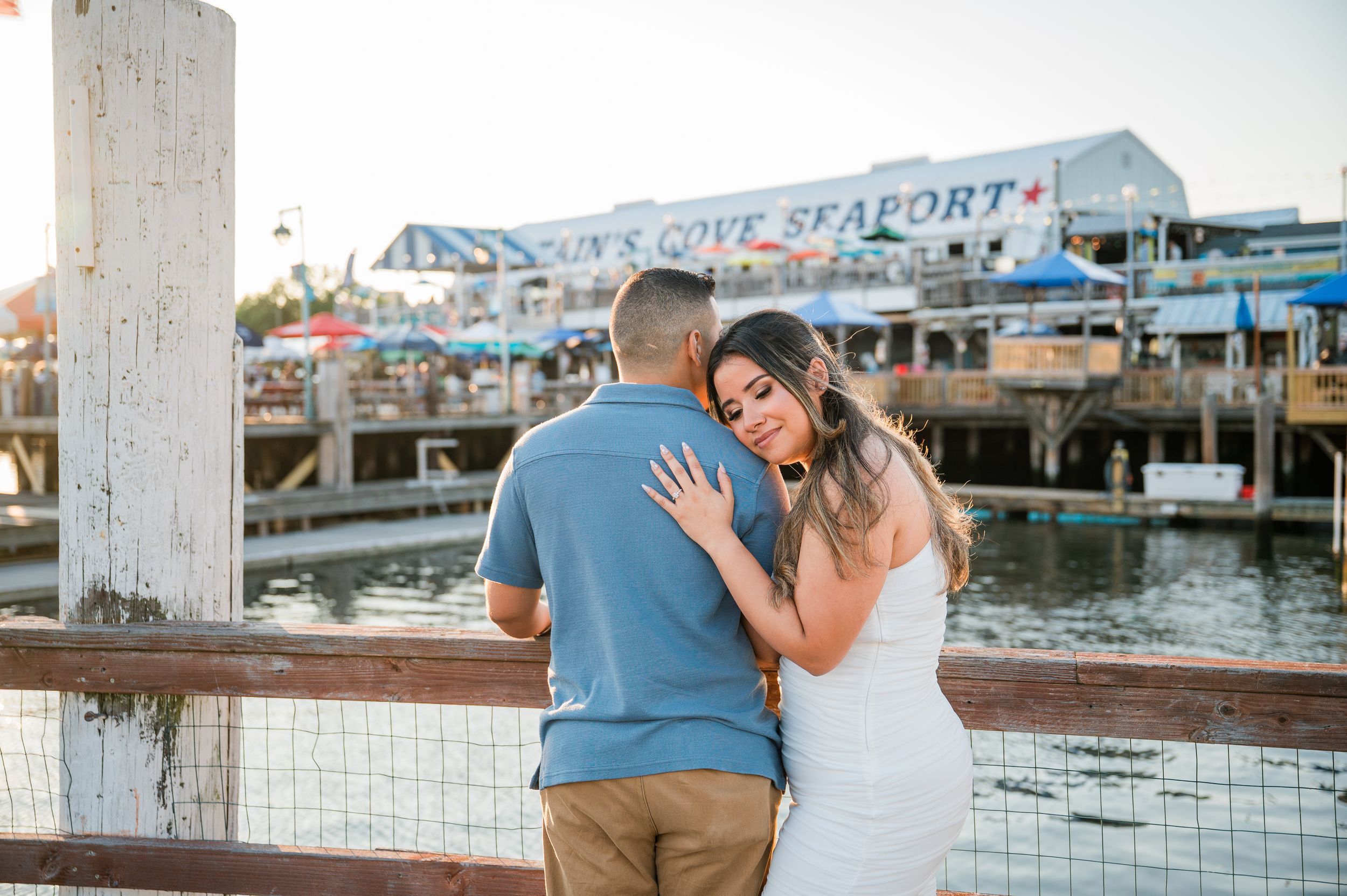 A couple embraces during a romantic sunset photoshoot at a waterfront marina with boats in the background in Captains Cove, Bridgeport, CT.