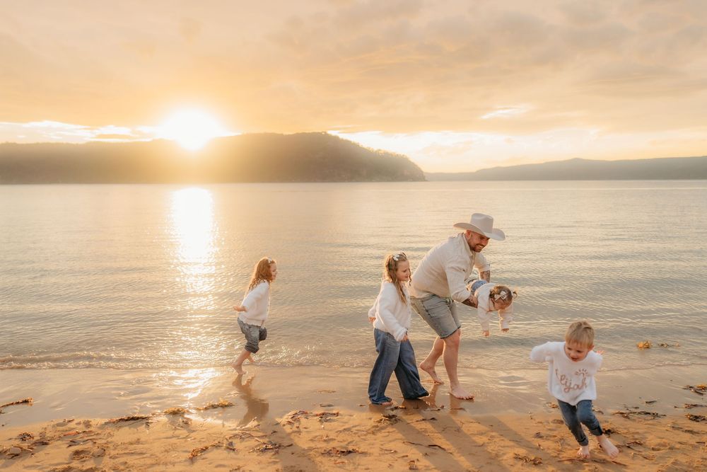 Family plays and laughs together on a sandy beach during a vibrant sunset, during family photography session.