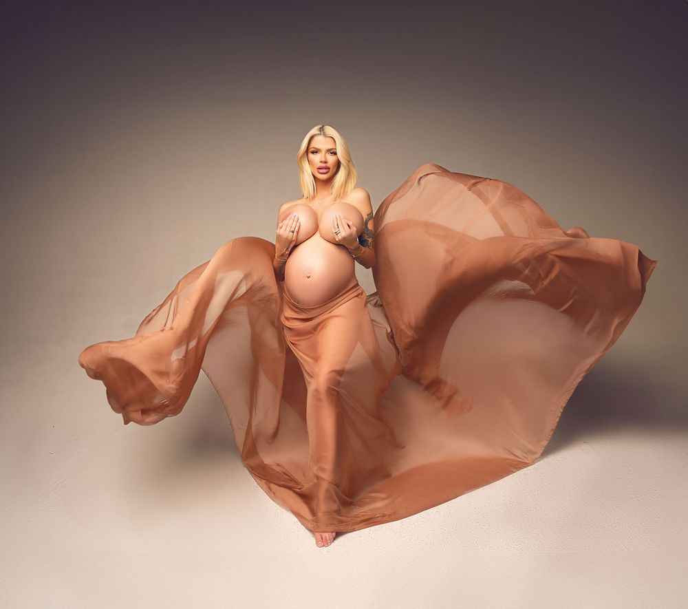 Maternity photo with flowing peach fabric against neutral studio backdrop.