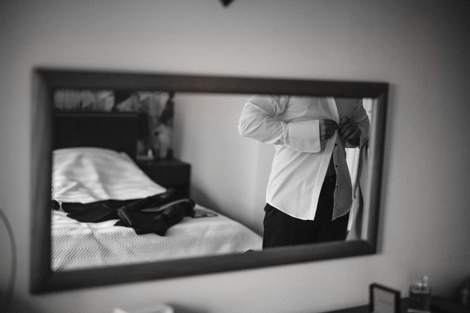 Black and white reflection of wedding preparations in bedroom mirror.