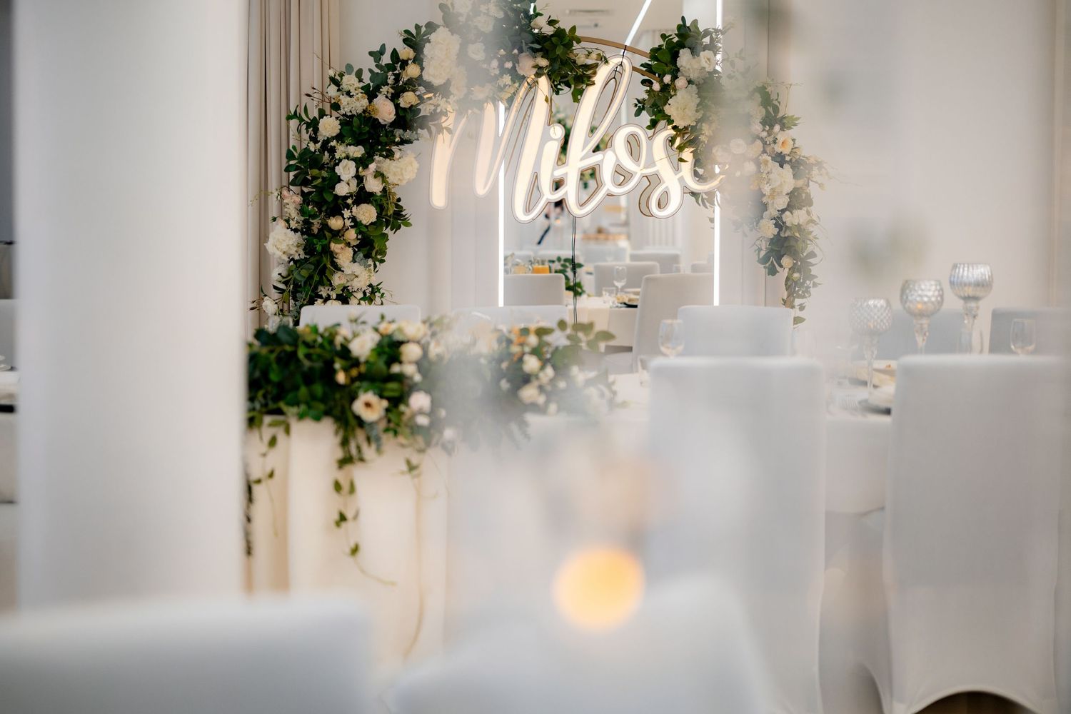 Elegant wedding reception decor featuring a neon 'Mrs' sign surrounded by white flowers and greenery.