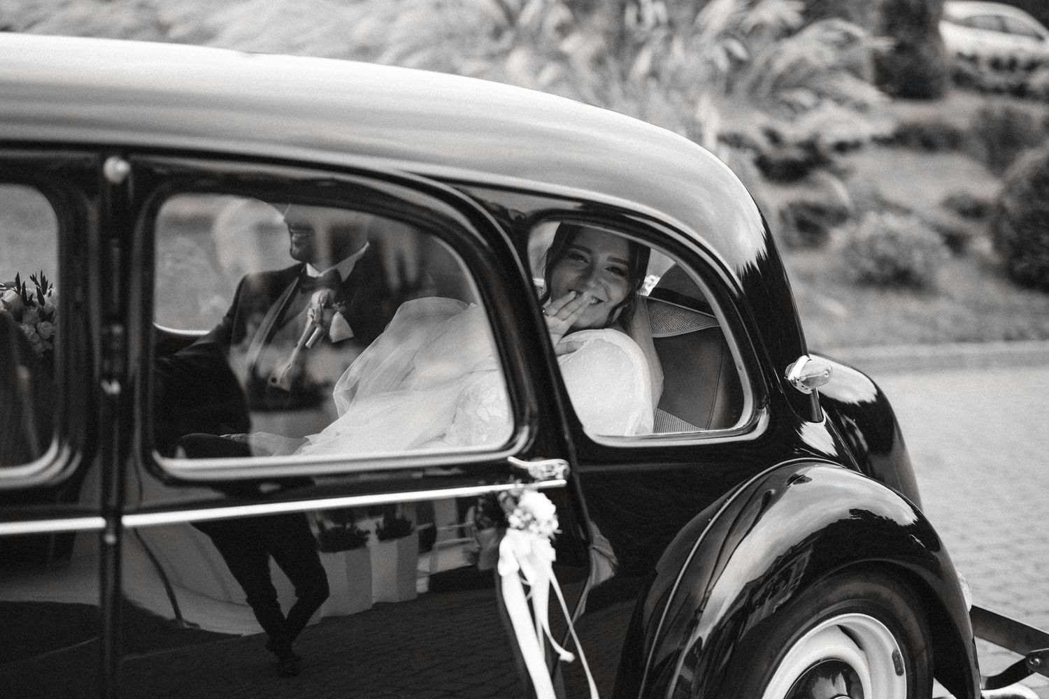 A classic vintage black car decorated for a wedding with a bride visible through the window.