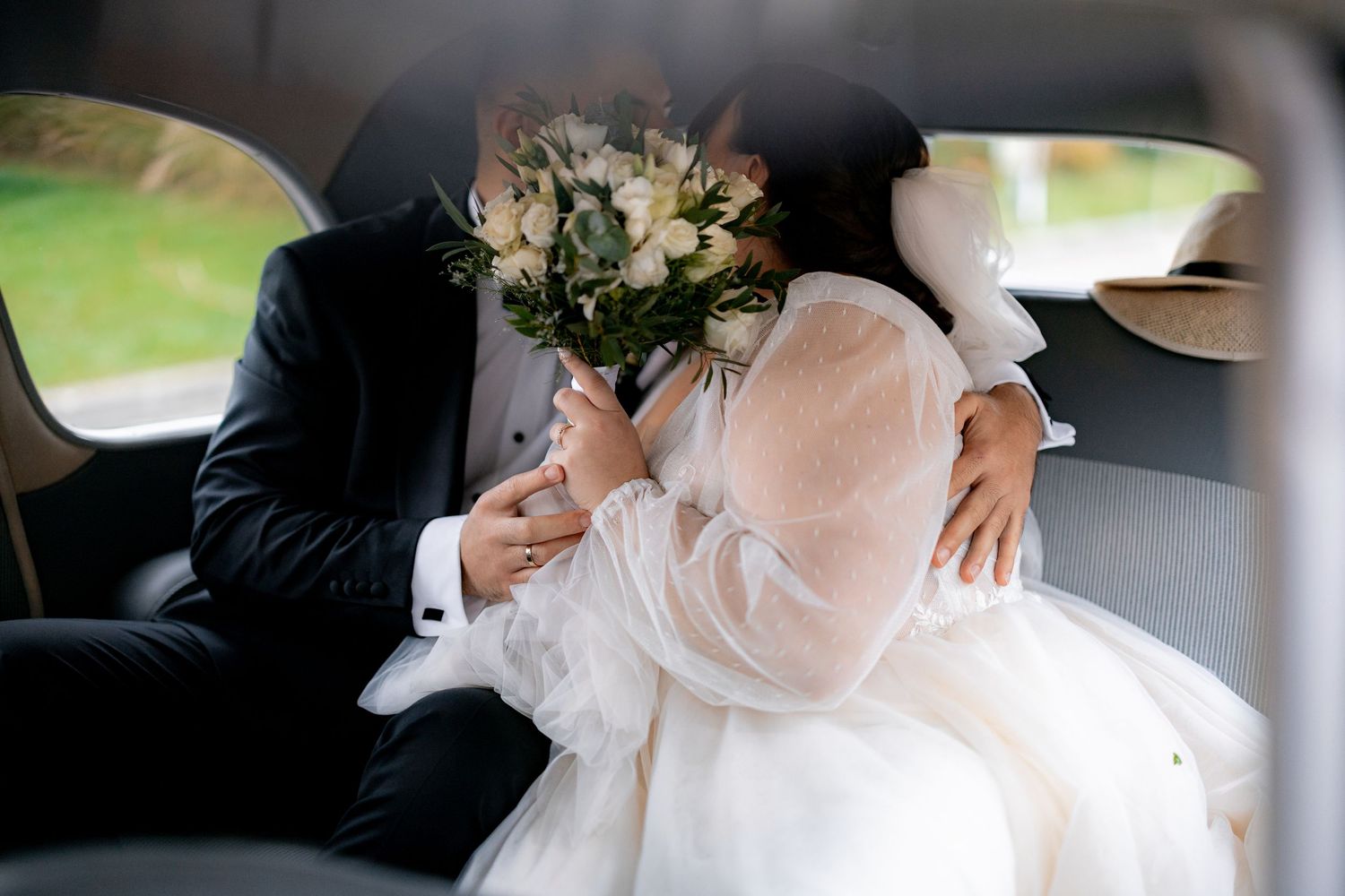 A wedding bouquet of white flowers rests on a flowing white dress inside a car.
