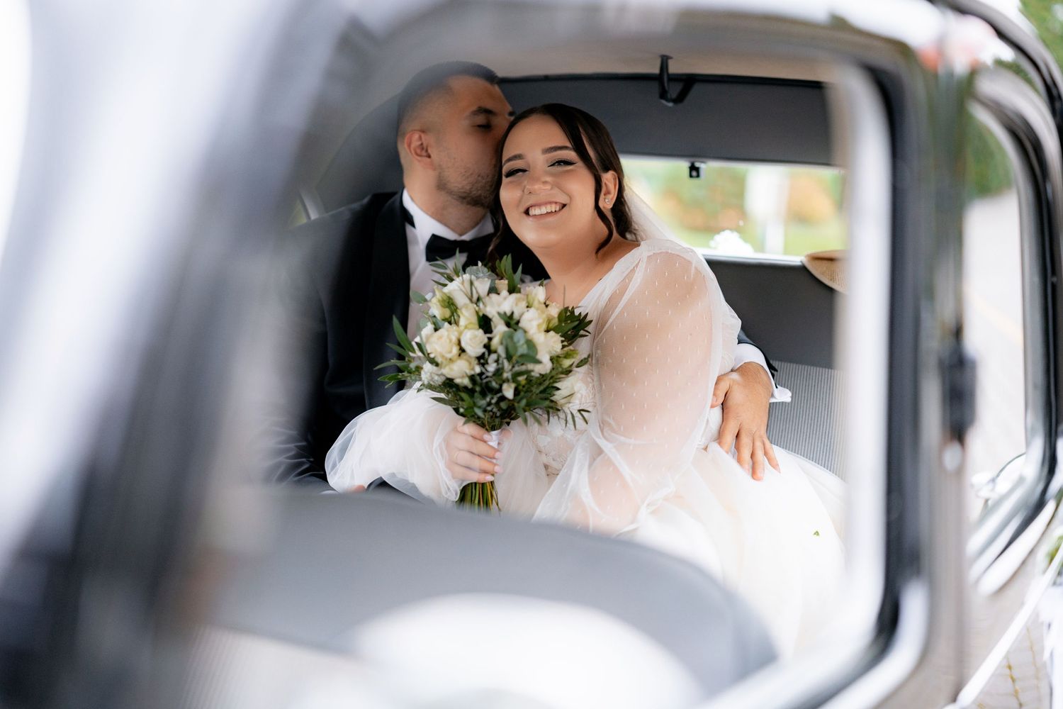 A joyful moment captured through a car window during wedding transportation.