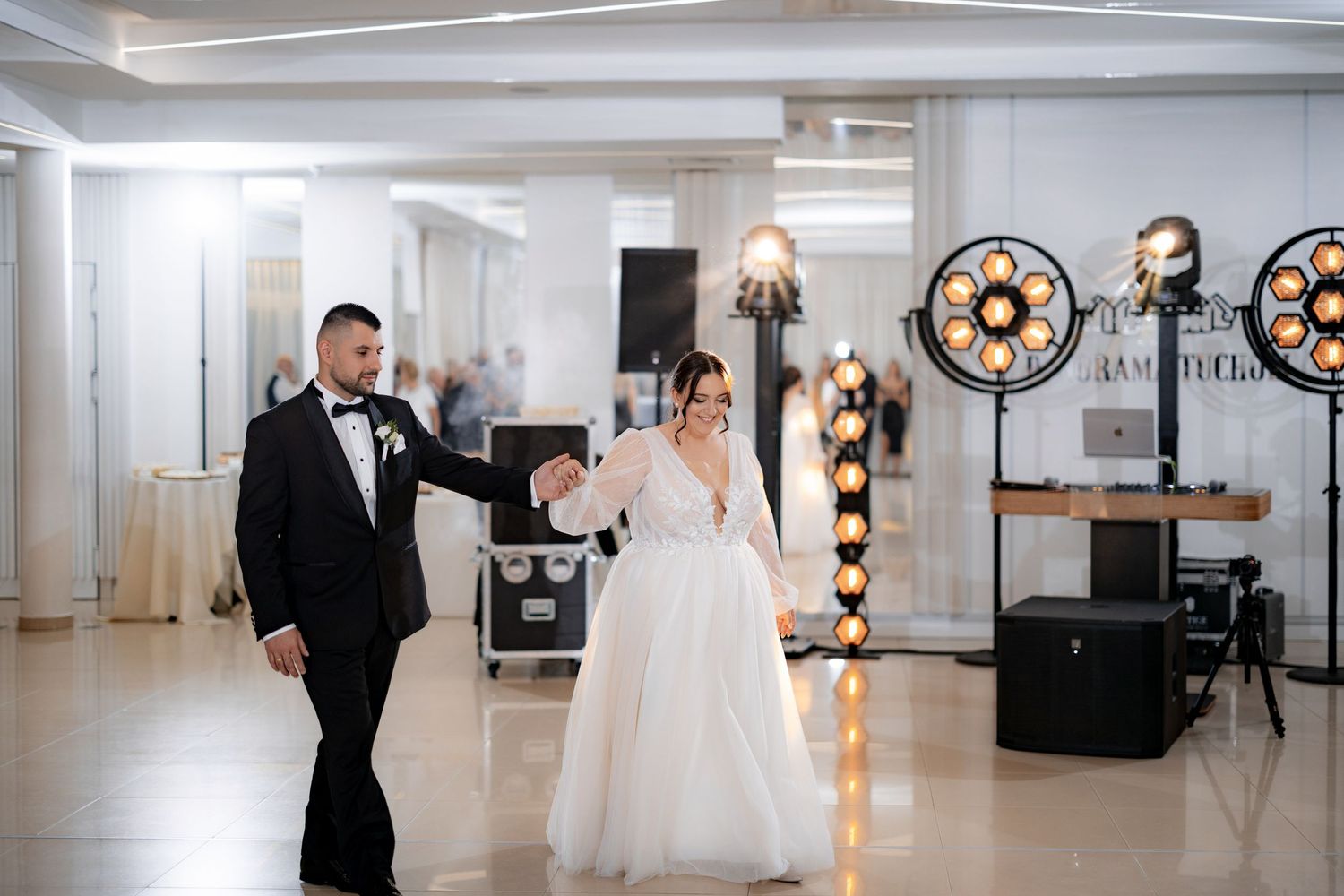 A couple enters their reception venue decorated with industrial-style lighting fixtures.