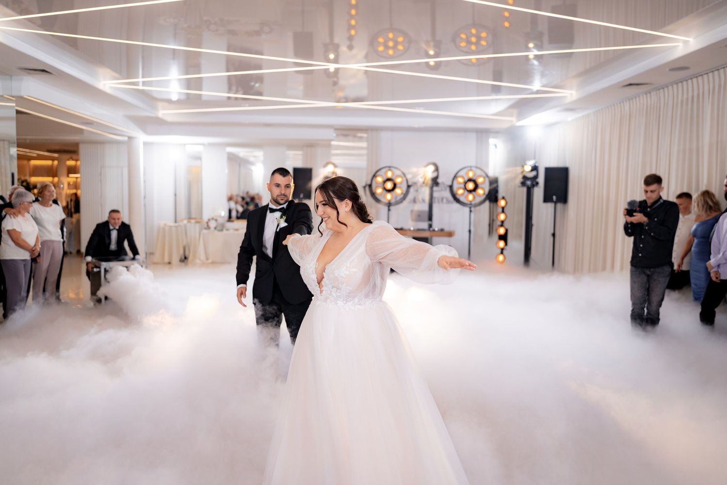 A couple performs their first dance on a misty dance floor with dramatic lighting at their wedding reception.