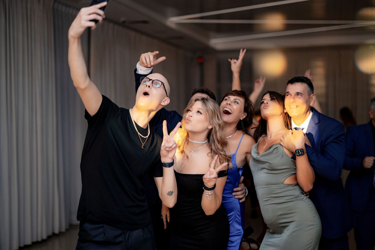 Party guests taking selfies and celebrating with drinks on the dance floor.