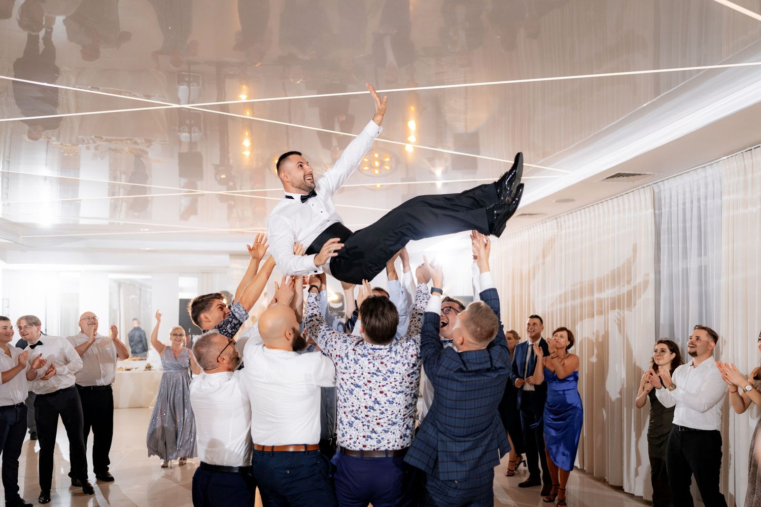 Wedding guests lift someone in celebration during a reception party.