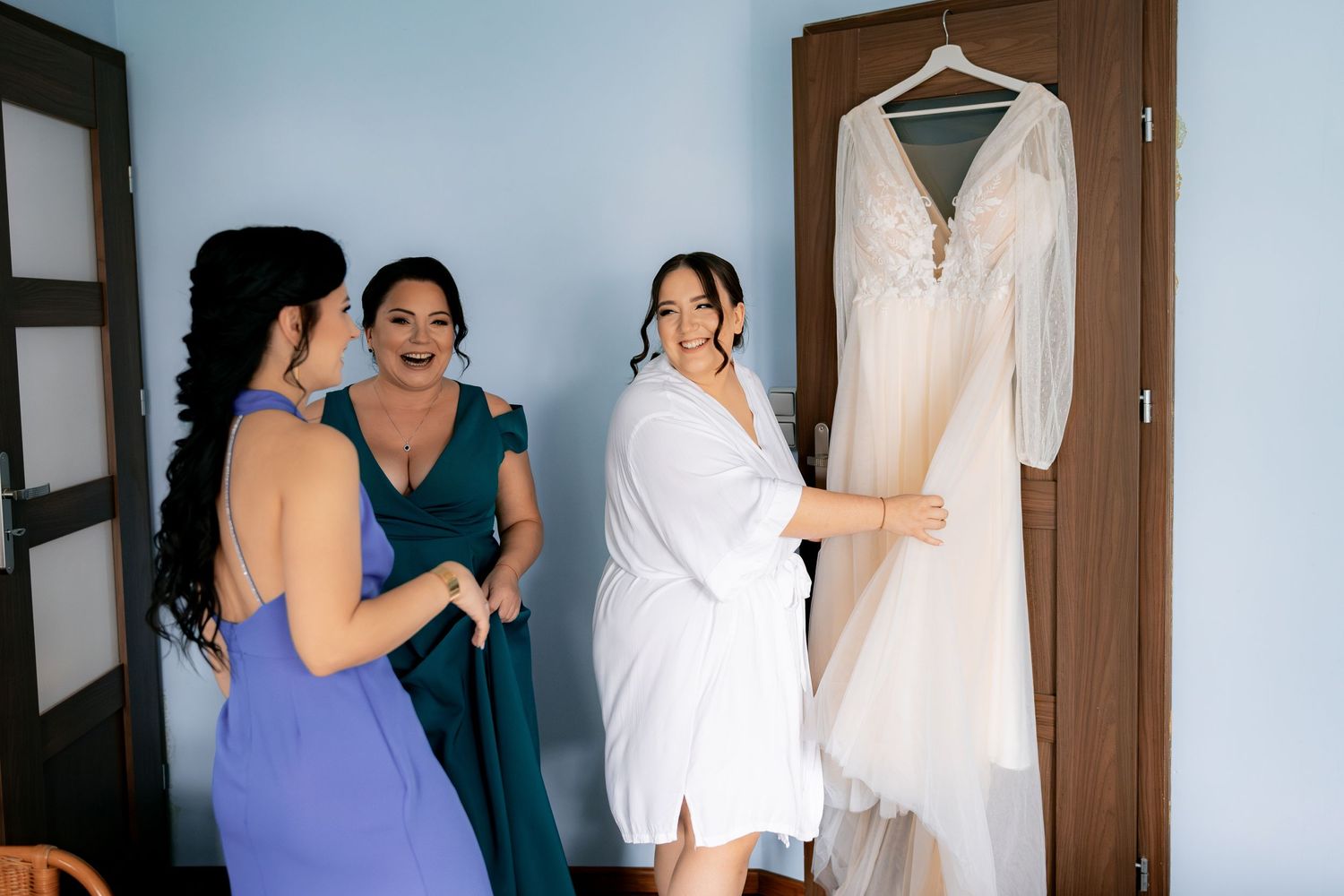 Bridesmaids in blue dresses helping with wedding gown preparations.
