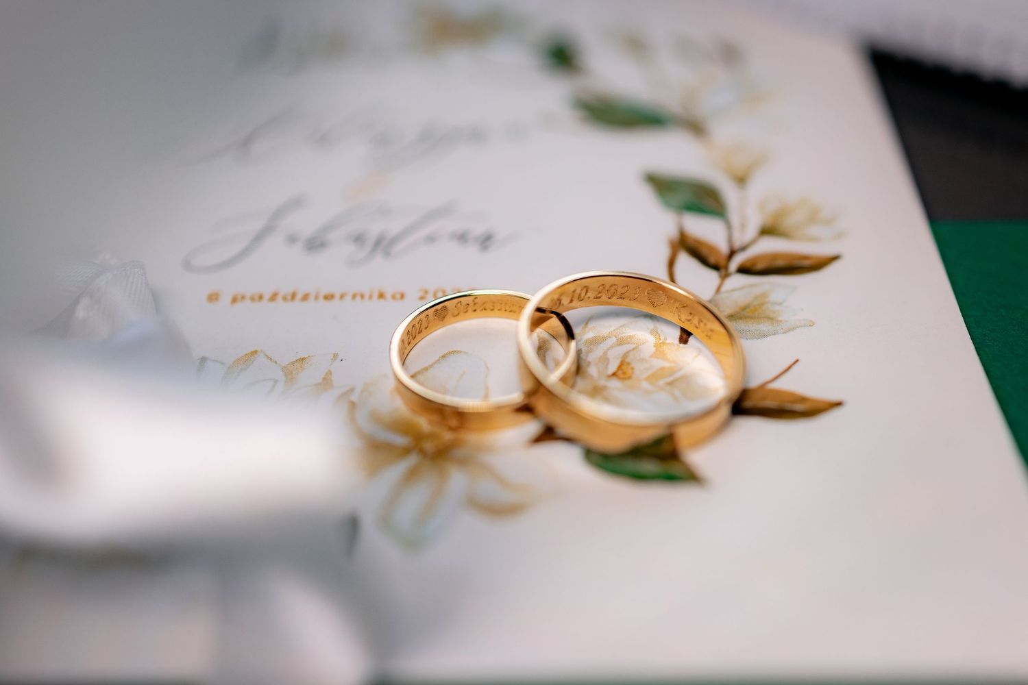 Two gold wedding rings resting on elegant floral invitation.