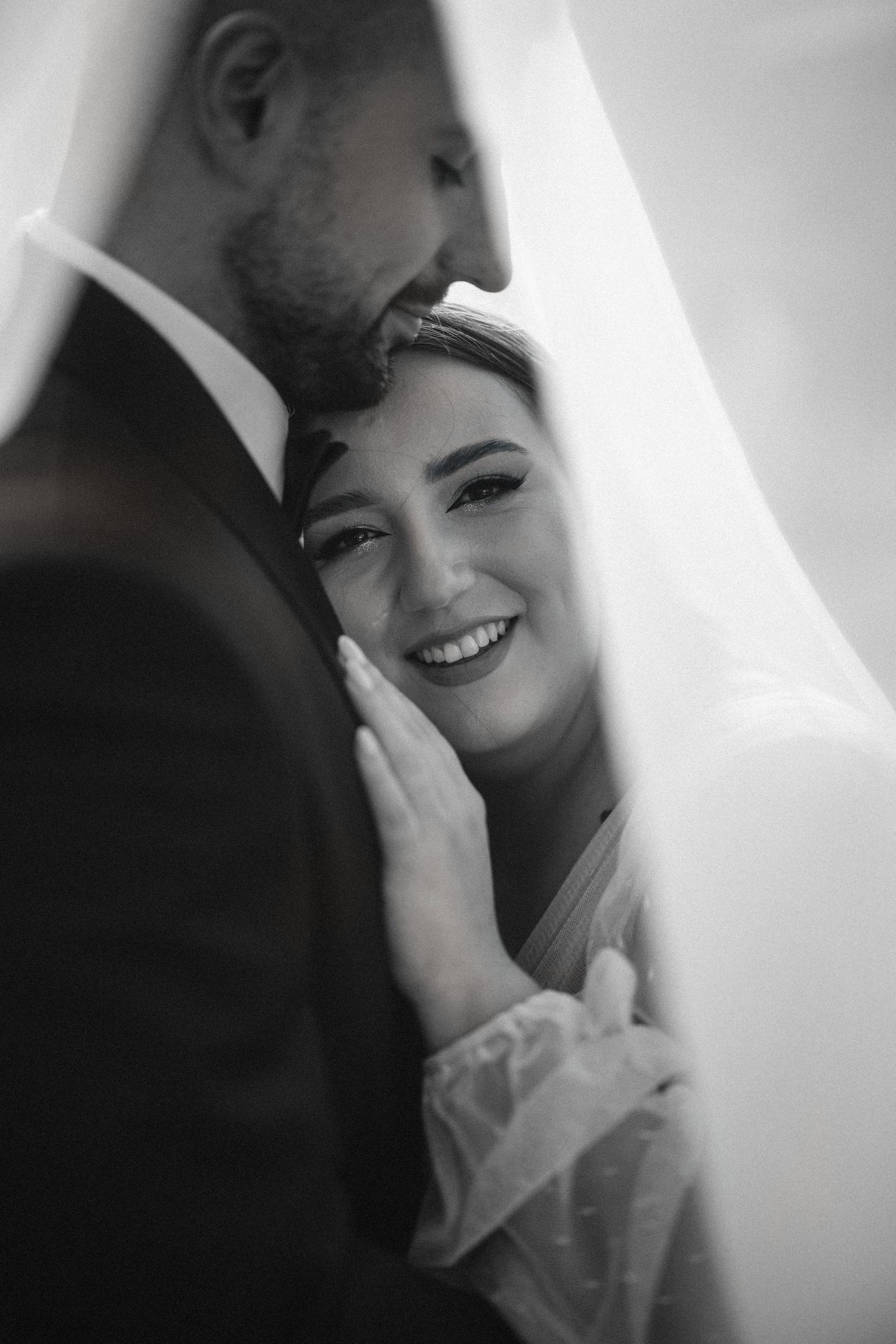 Black and white portrait of newlyweds sharing an intimate moment under a veil.