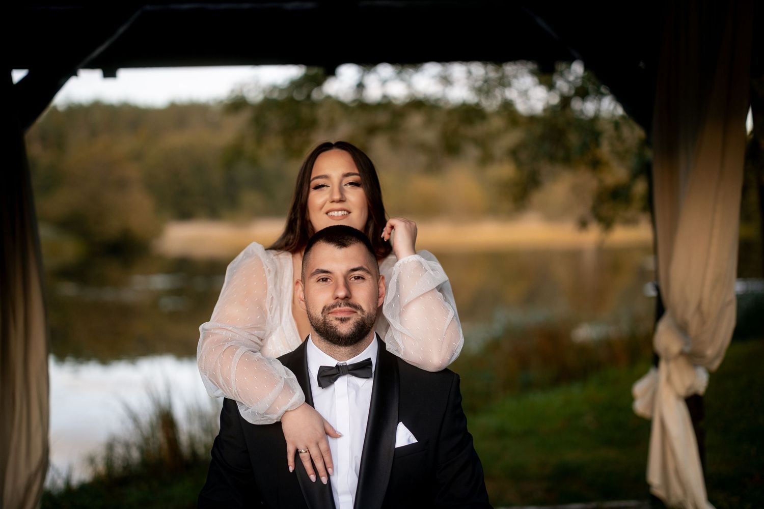 Artistic portrait of couple in wedding attire with moody outdoor backdrop.