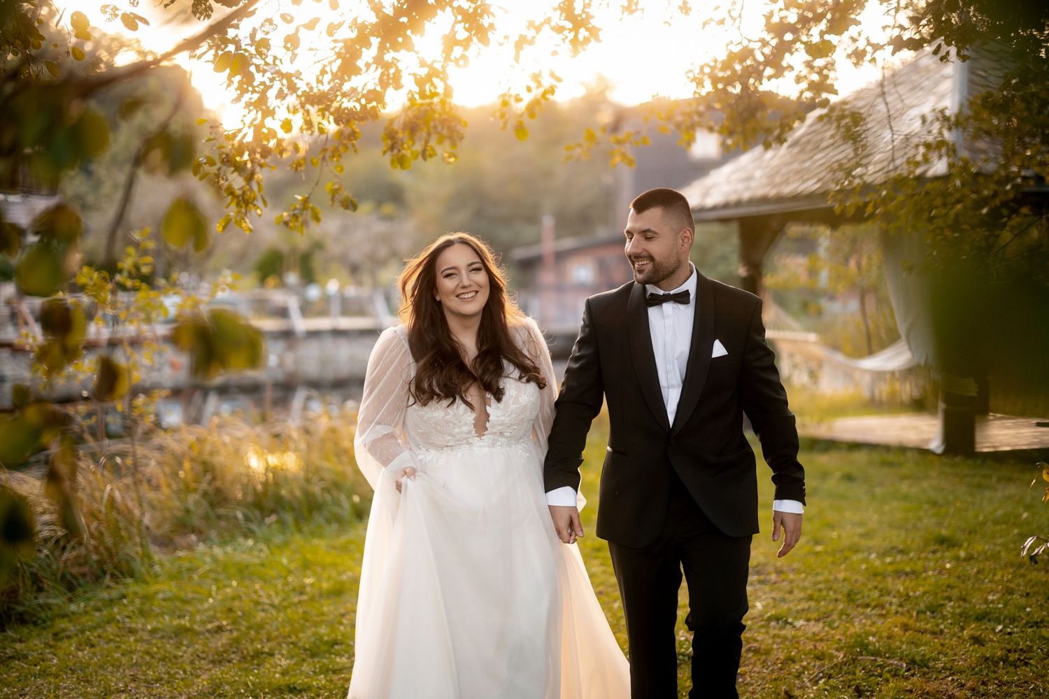 Couple walking through sunlit garden path during golden hour in wedding attire.