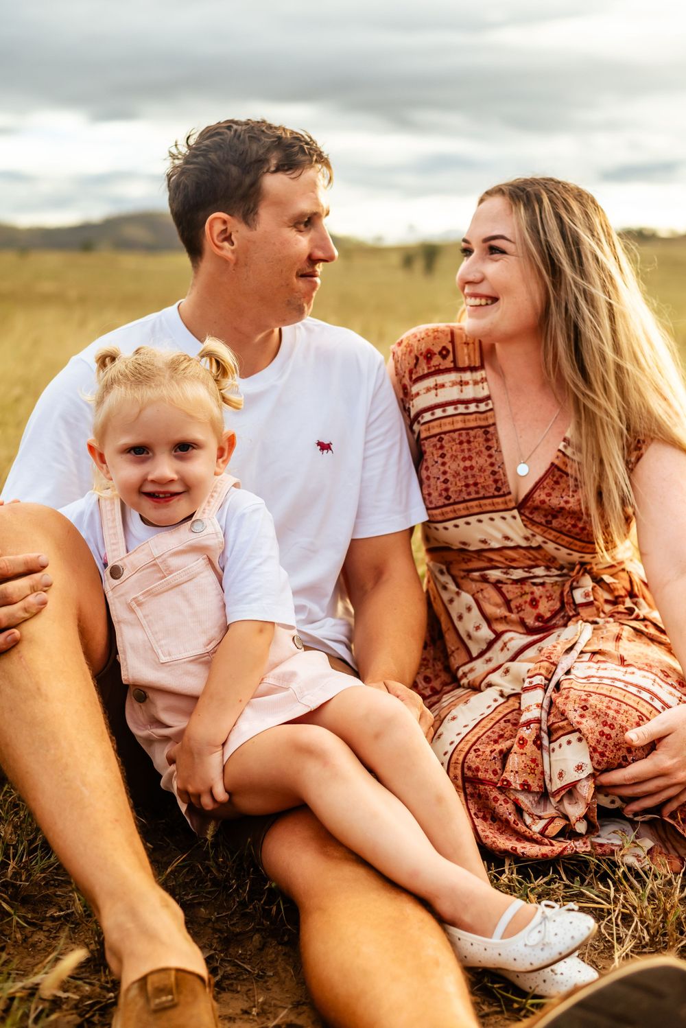 Close-up portrait of a family sitting together and smiling in a sunny meadow.