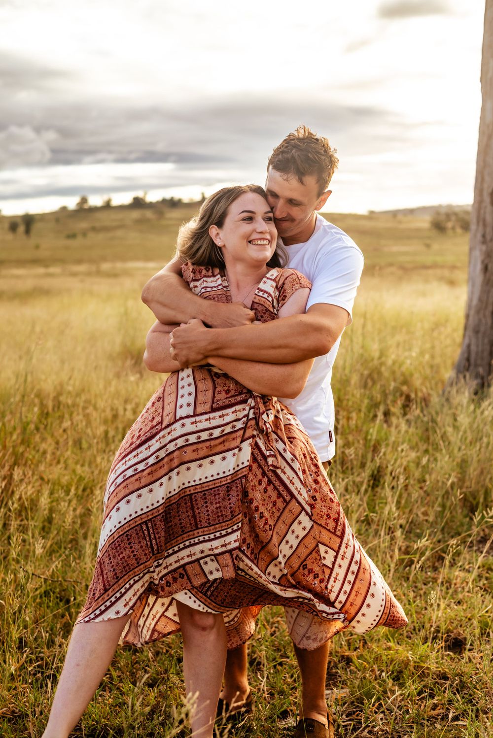 A romantic embrace in a sundrenched field with mountains in the background.