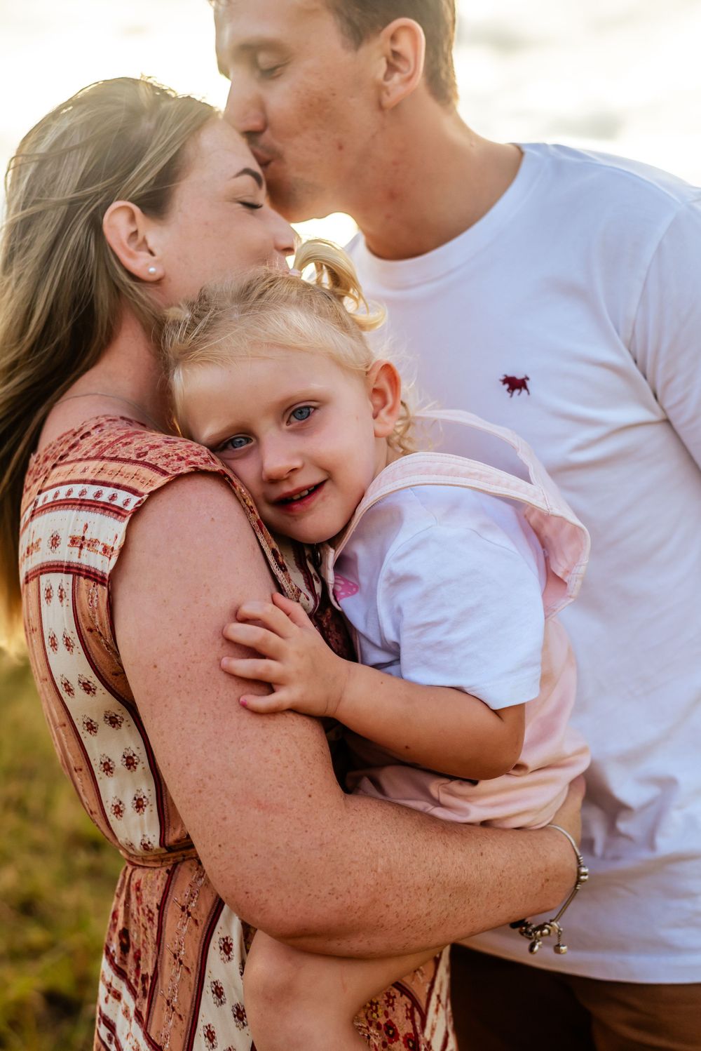 Intimate family moment with parents kissing while holding their smiling child.