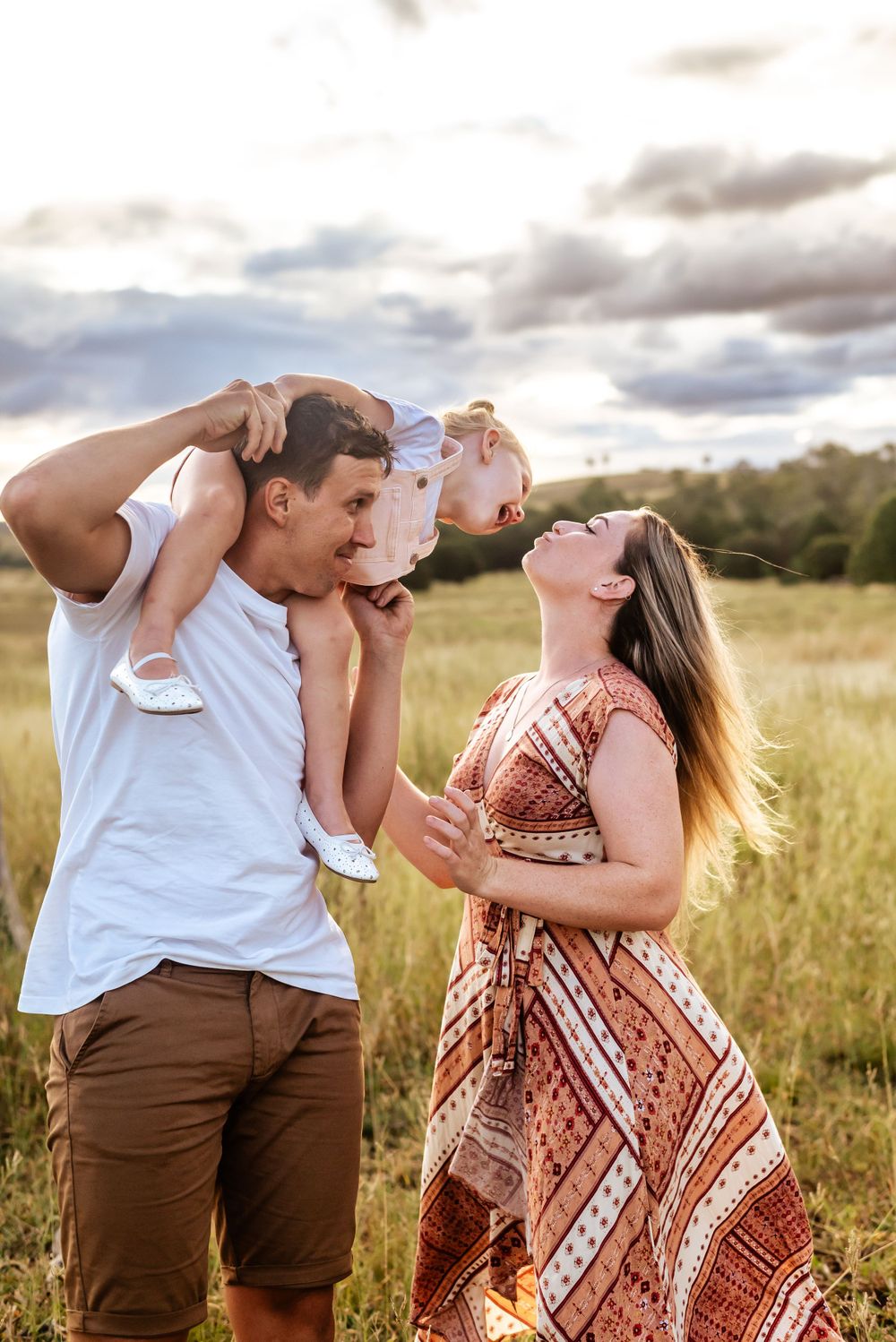 Parents playing with their child in a sunlit field, lifting them up playfully.