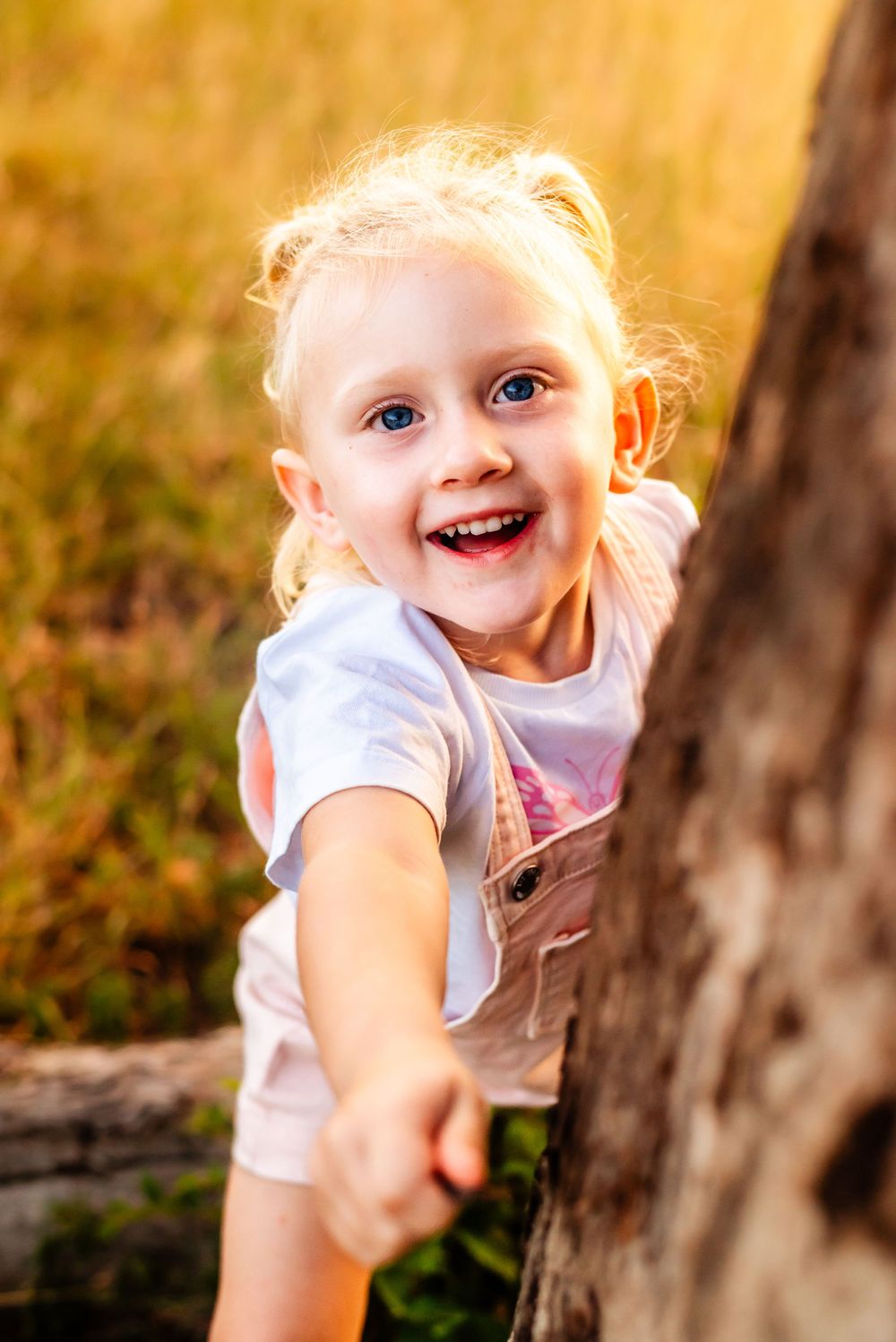 Close-up of a joyful child with blonde hair playing near a tree trunk.
