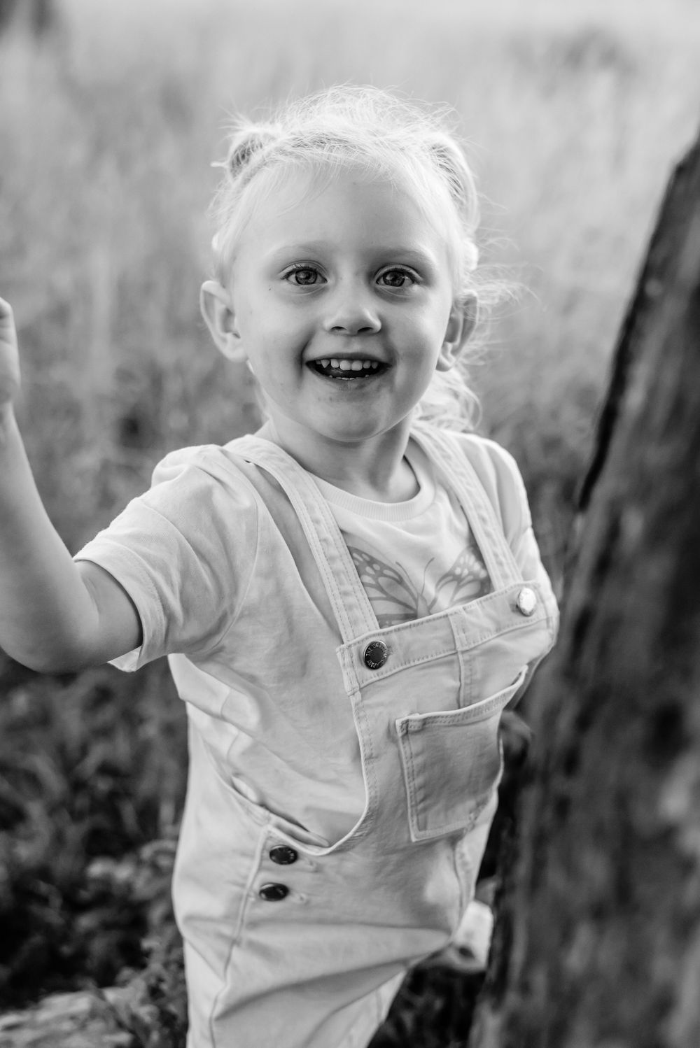 A joyful child in white overalls playing outdoors in black and white.