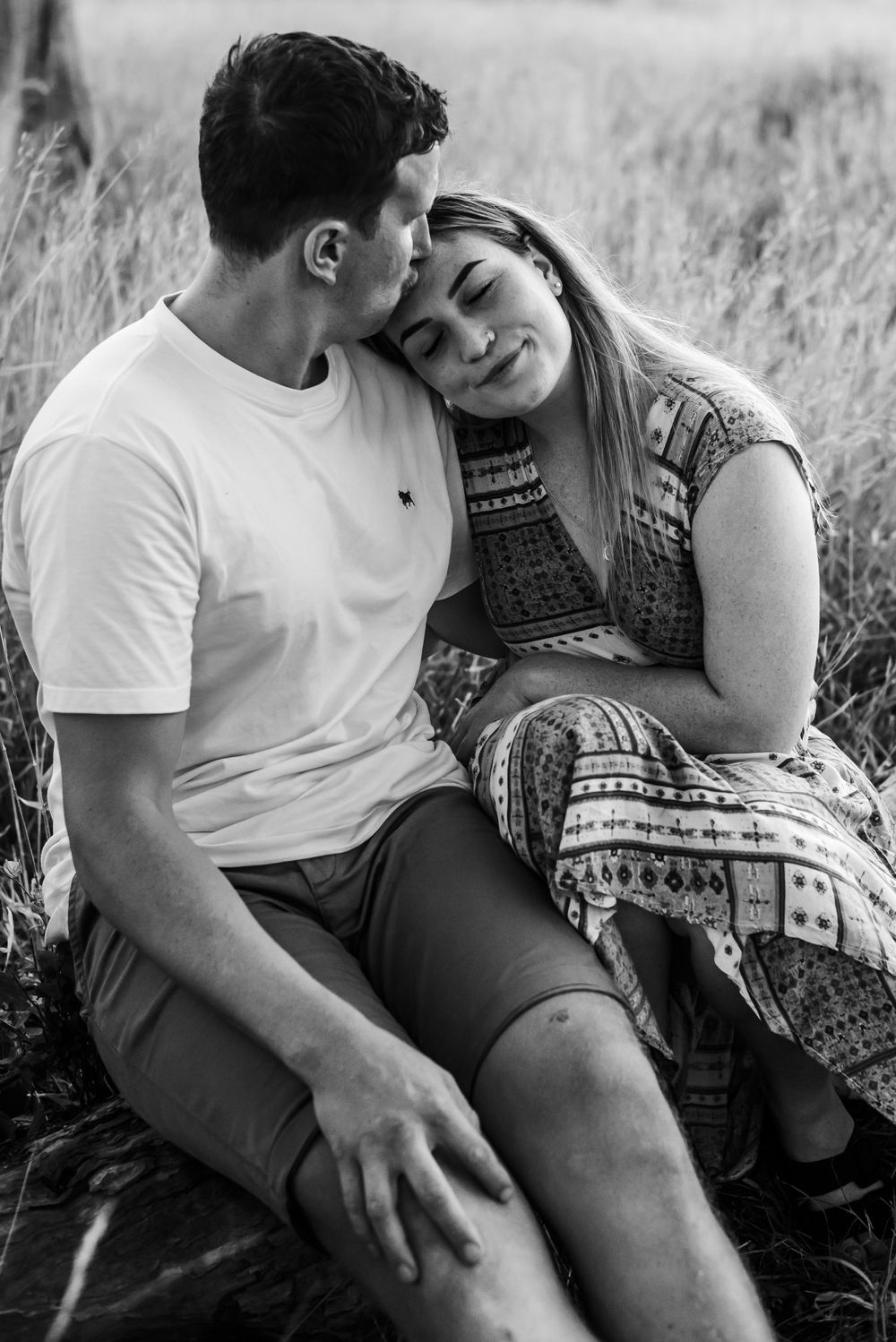 An intimate black and white portrait of a couple sharing a tender moment in tall grass.