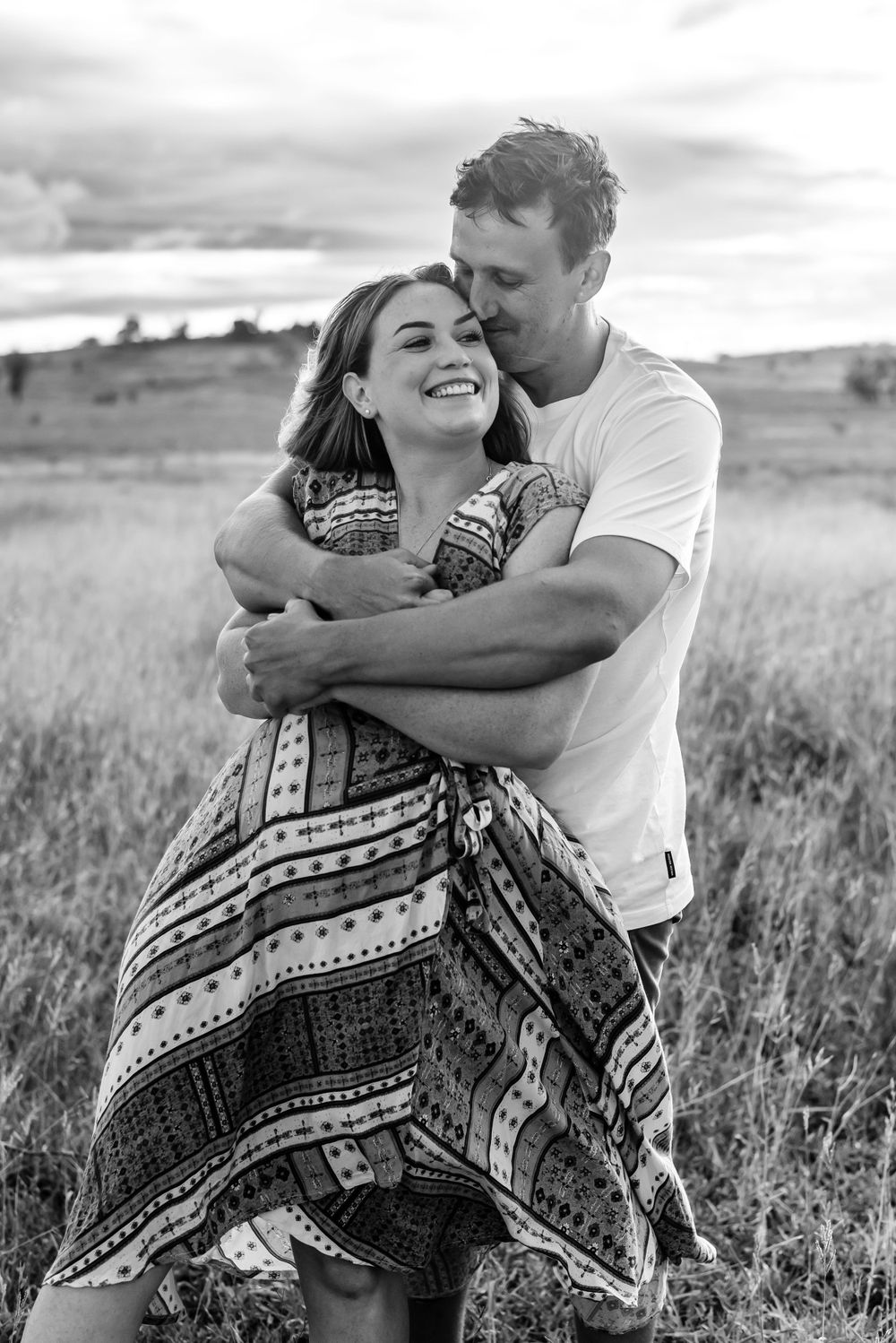A romantic black and white portrait showing a loving embrace in a rustic outdoor setting.