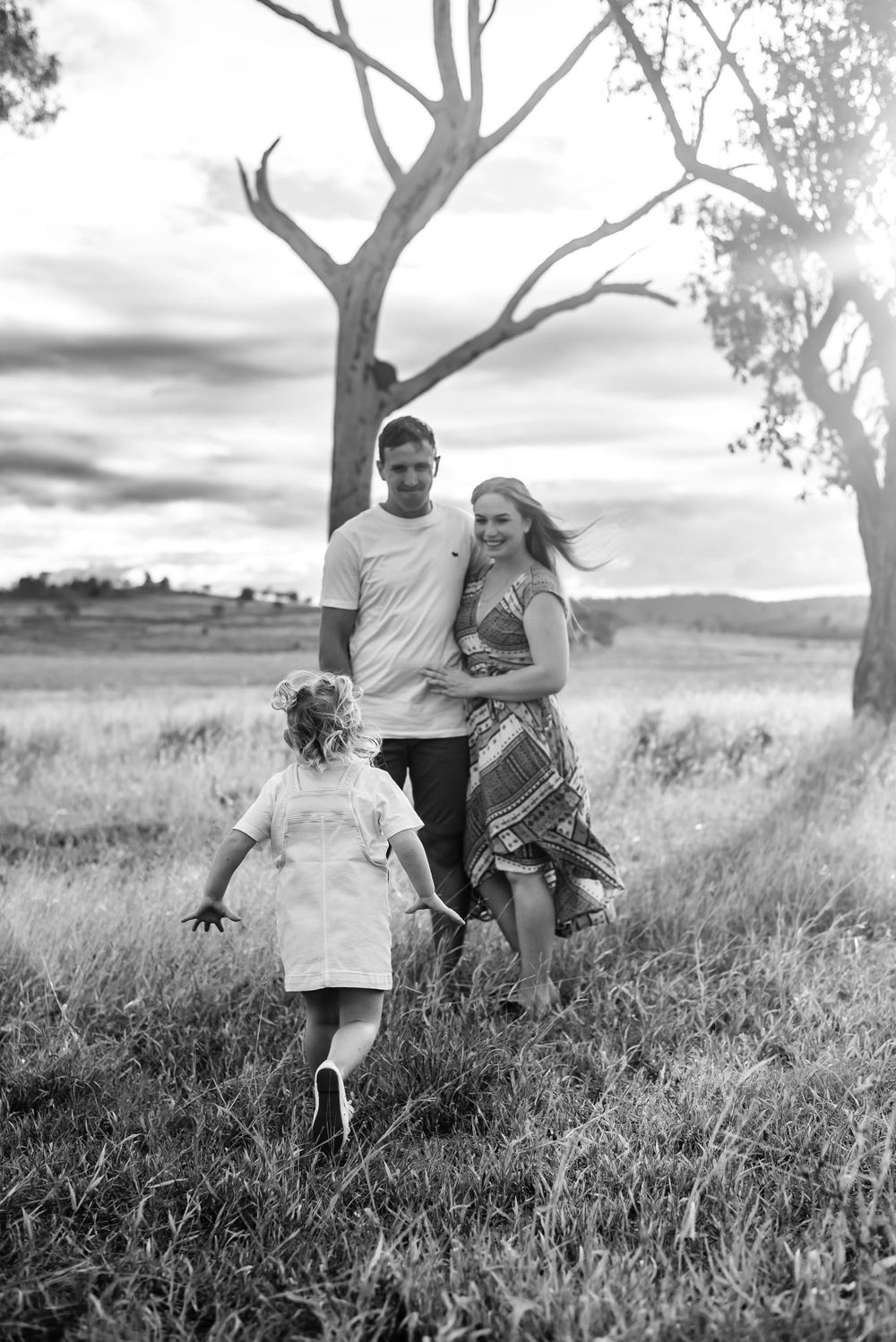 A black and white family portrait in a field with trees silhouetted against the sky.