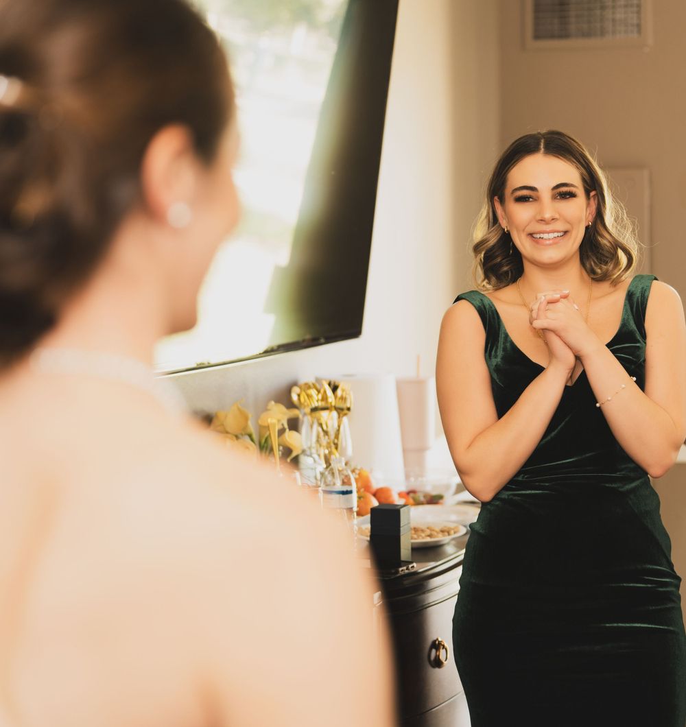 Woman in black velvet dress reacts emotionally while getting ready in a bright indoor setting.