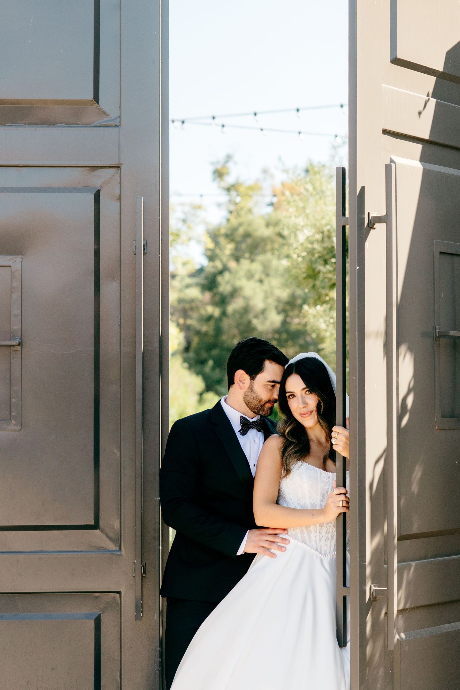 Newlyweds walk together on green lawn with palm trees and hedges in elegant tropical garden setting.