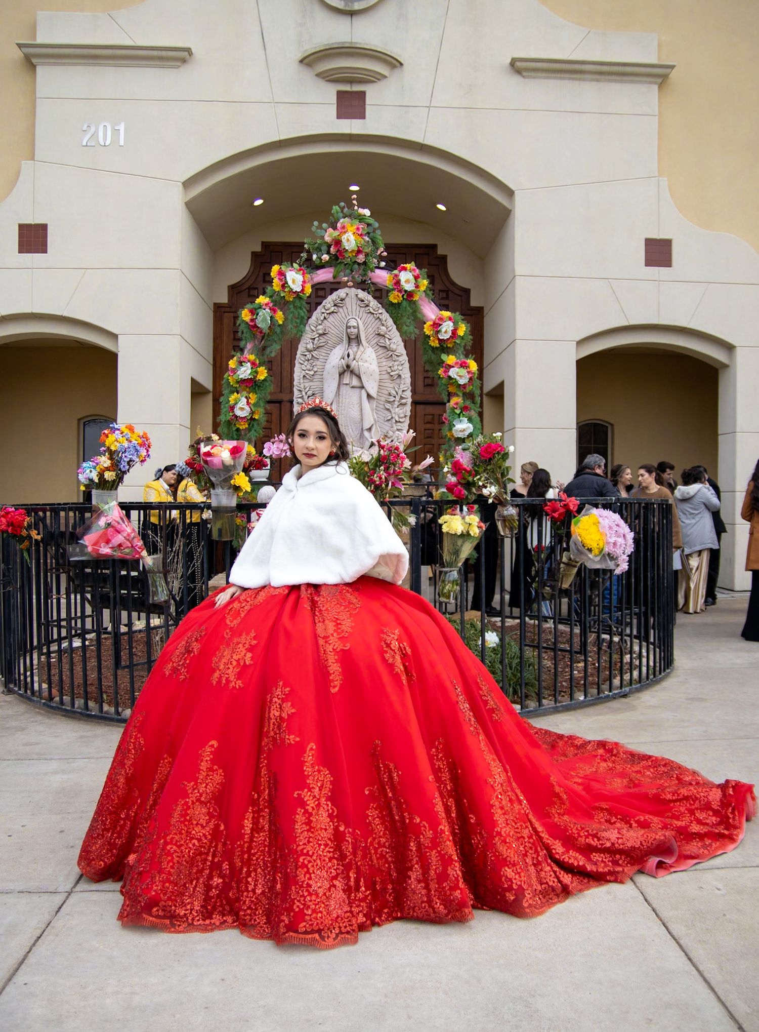 A celebrant in a dramatic red and white ball gown poses in front of an ornate religious shrine.