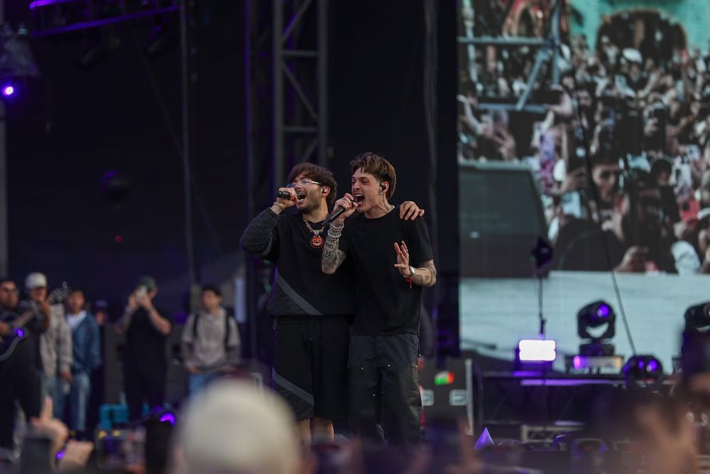 Two performers energetically singing together on stage with a large screen display in the background.