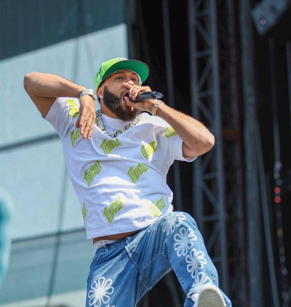 Performer in white t-shirt with neon green accents and green cap energetically moving on outdoor stage.