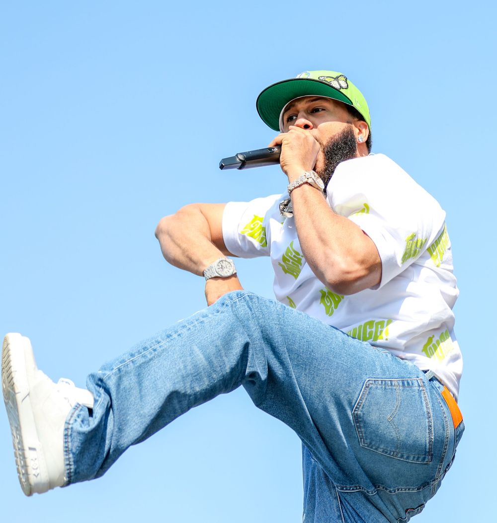 Performer in white shirt and jeans executing energetic dance move against blue sky.