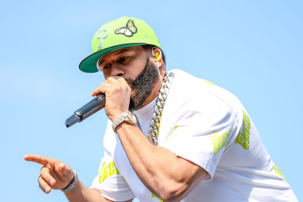 Performer in casual attire gesturing animatedly during outdoor concert performance.
