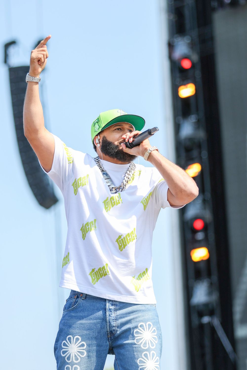Stage performer in white t-shirt and jeans raising arms during outdoor show.