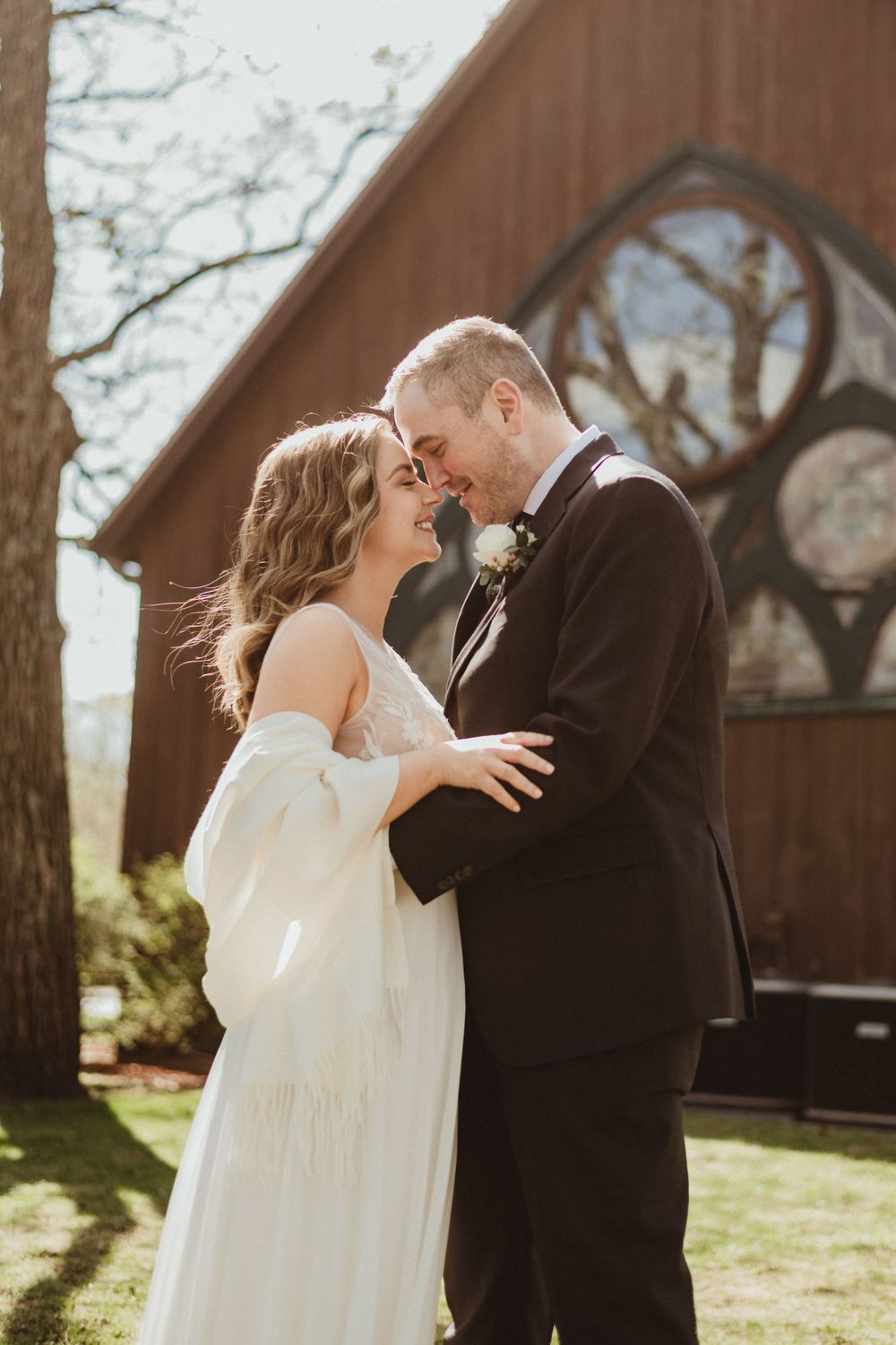 Intimate wedding moment captured outside wooden chapel with natural sunlight.