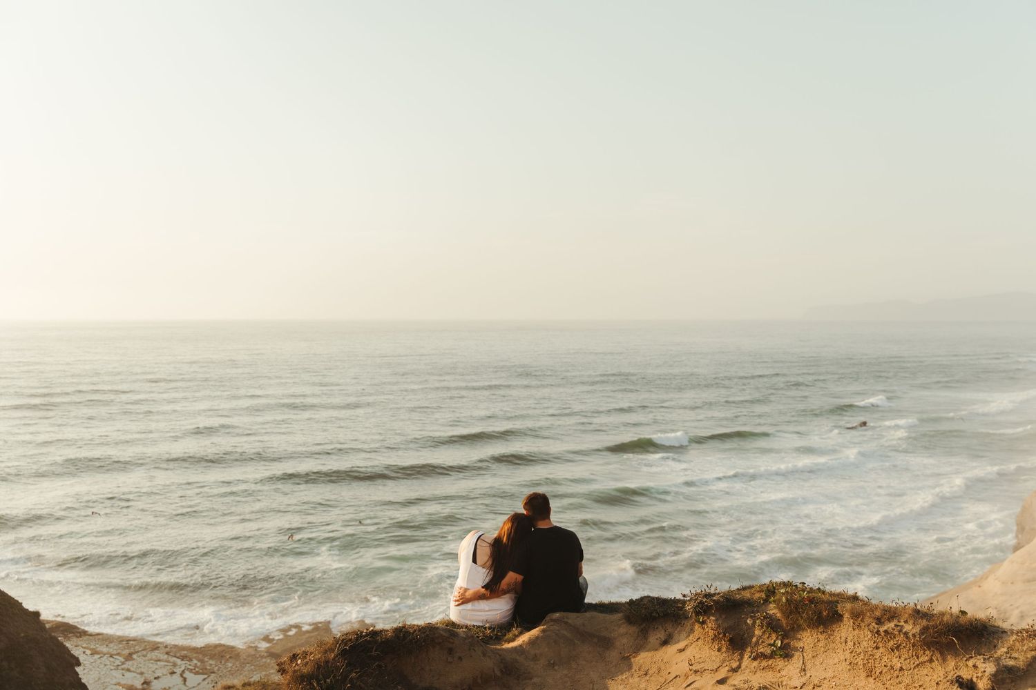 Two people sharing an intimate moment on a picnic blanket in a wooded setting.