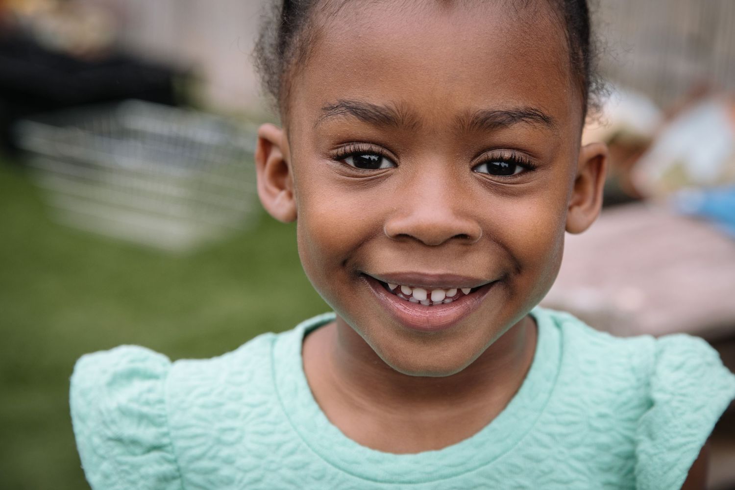 A bright outdoor portrait showing a genuine smile while wearing a mint green top.