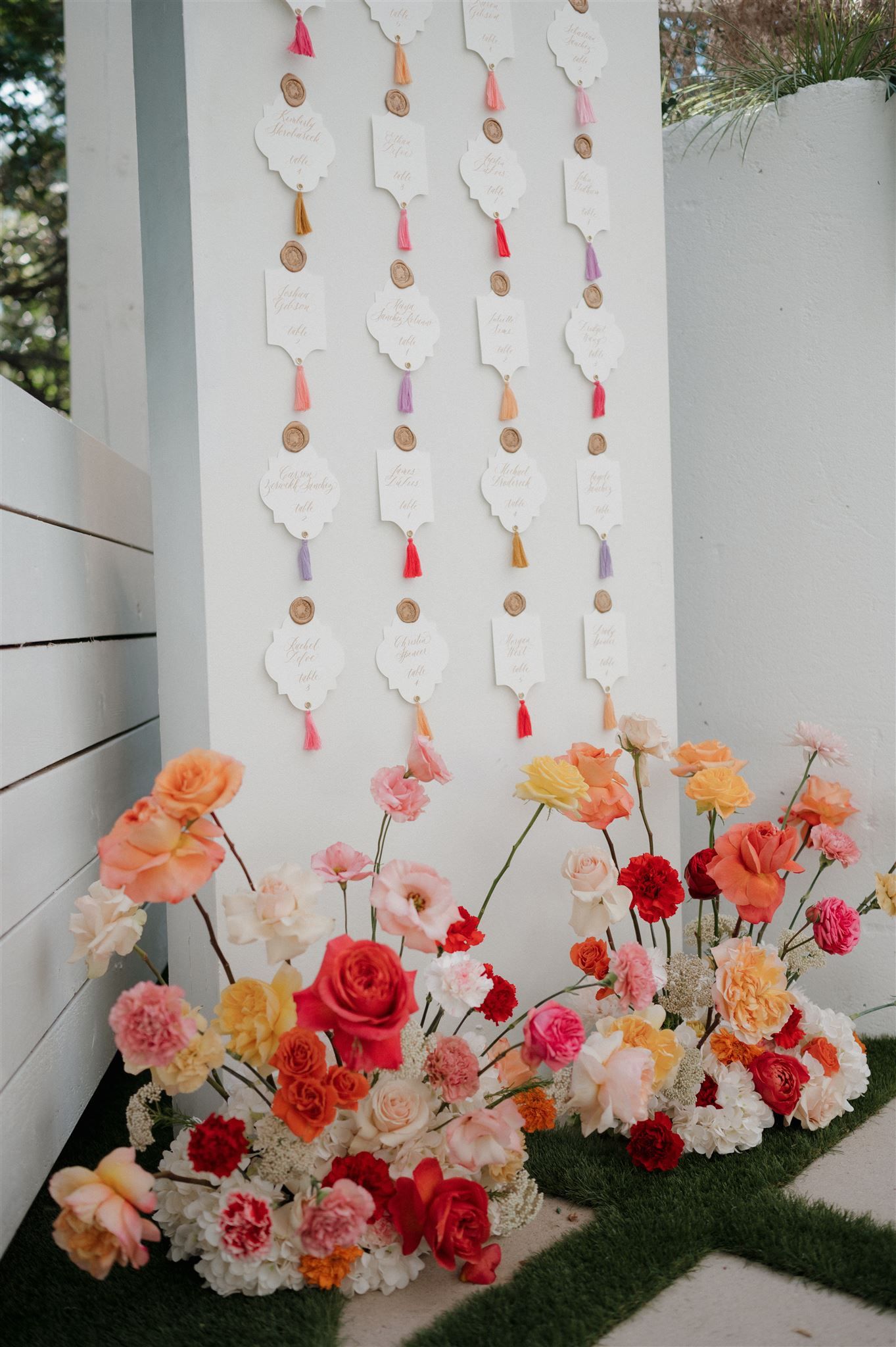 Decorative white tags with tassels hang on a wall above a colorful floral arrangement of roses and carnations.