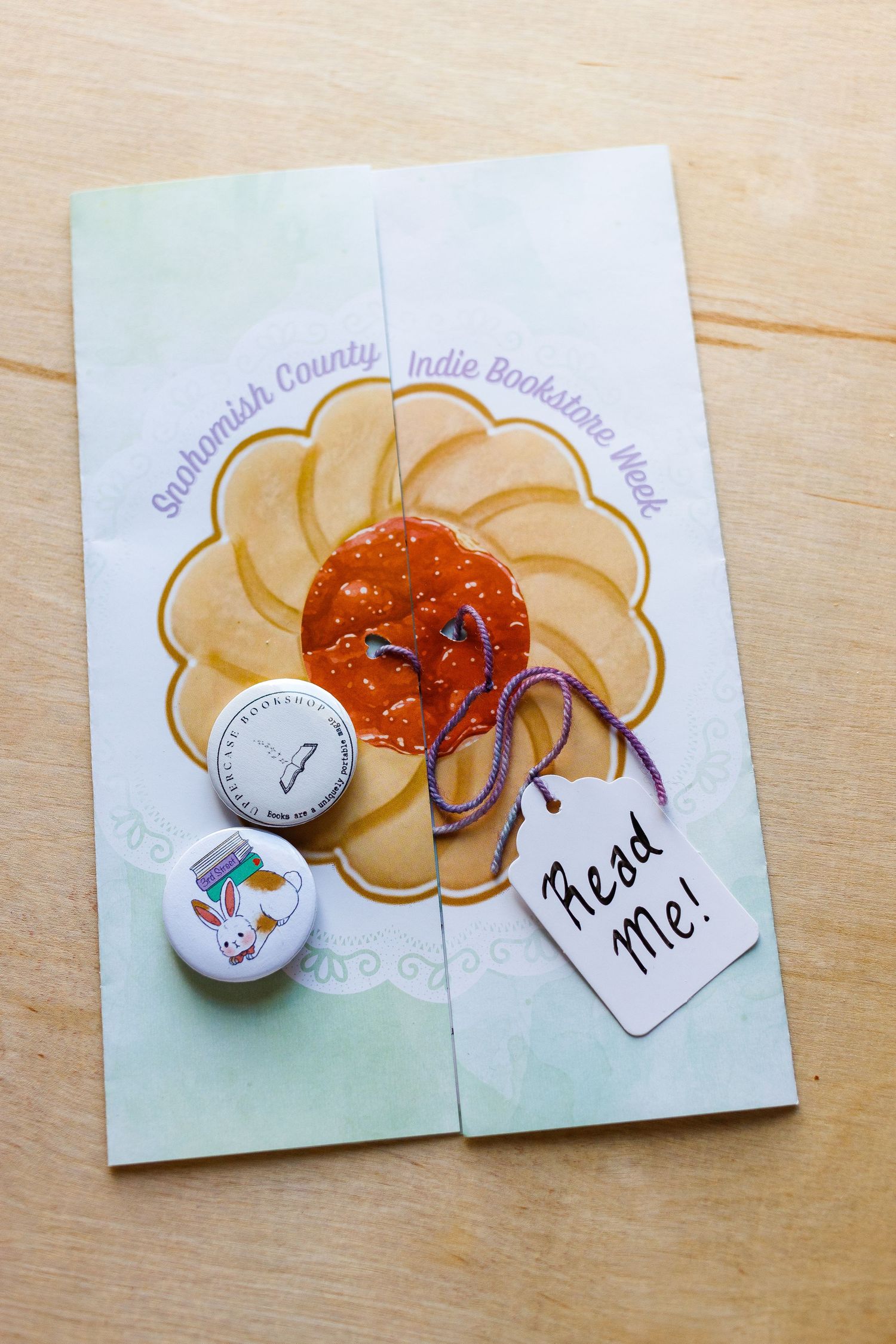 Artistic floral design card with orange center and purple ribbon on wooden surface.