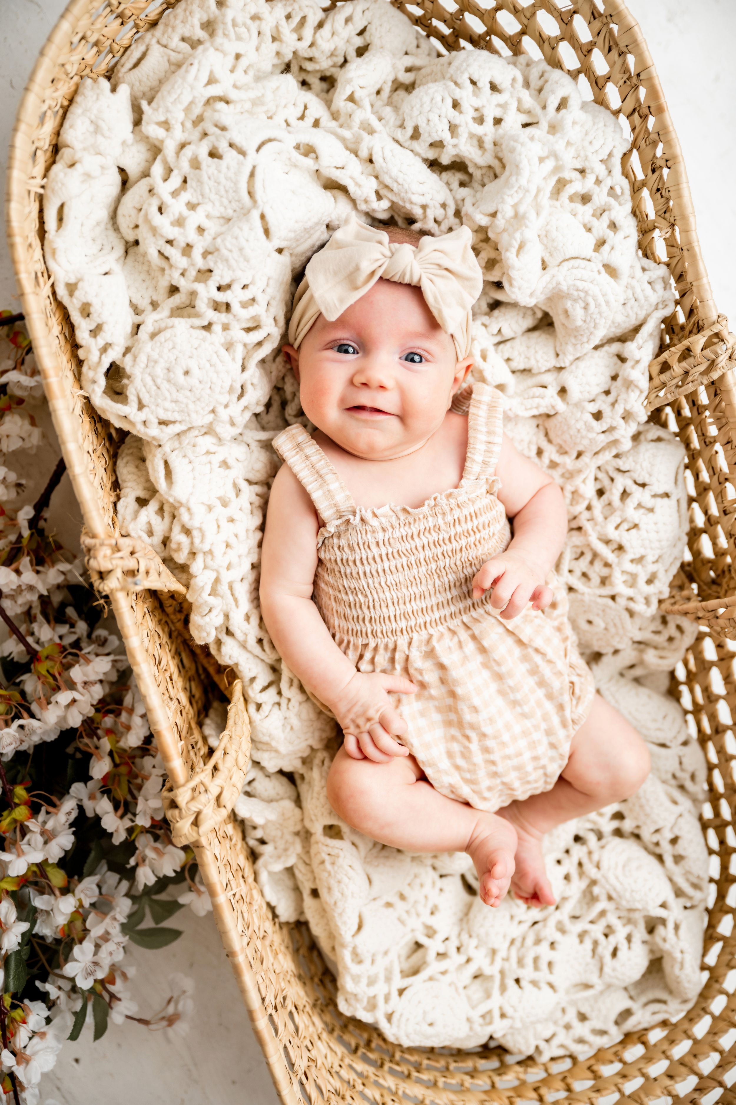 Baby portrait in cream-colored crochet outfit laying in vintage basket setting.