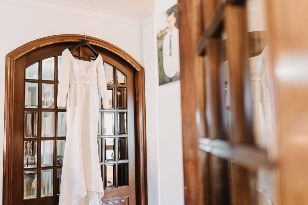 White wedding dress hanging in front of an arched wooden doorway.