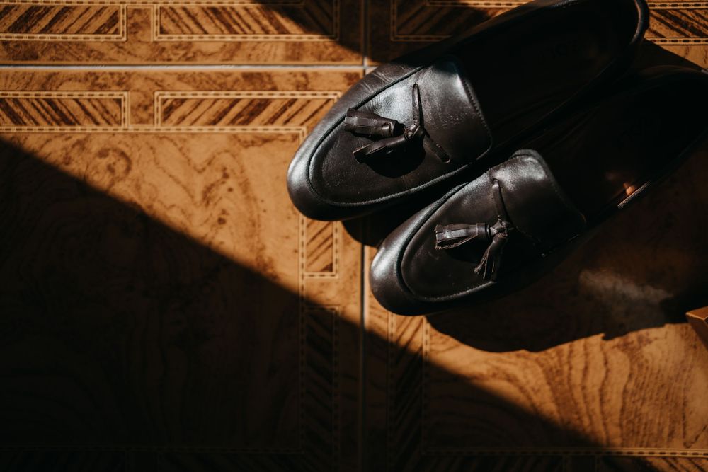 Shiny black formal shoes on patterned carpet with dramatic shadow and lighting.