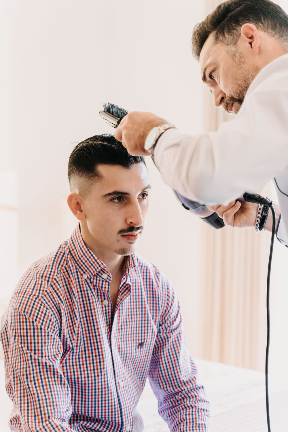 Barber styling client's hair with professional tools in a bright studio setting.