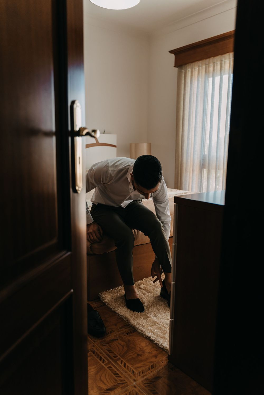 Person sitting in darkened room viewed through doorway with moody lighting.