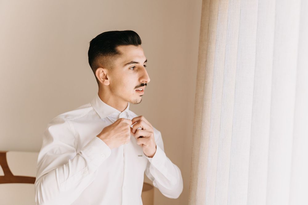Man in white dress shirt fixing his bow tie while getting ready.